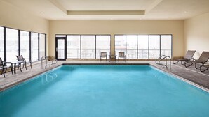 Una amplia piscina interior con vistas despejadas a través de grandes ventanales, rodeada de sillones de descanso y una pequeña mesa.