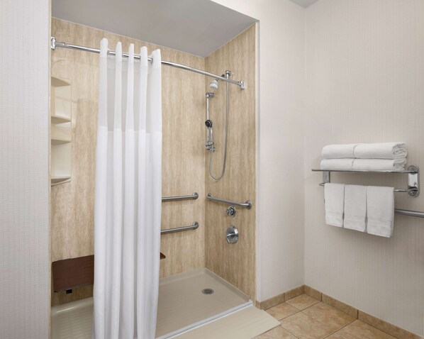 A shower area with a glass door, a showerhead, a handheld shower attachment, and a towel rack with towels.