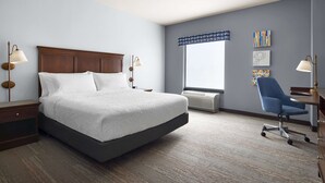 Habitación de hotel con una cama grande, un escritorio con silla, una ventana con vistas y obras de arte en la pared.
