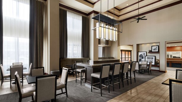 Un hall de hotel con zona de bar, asientos y un amplio ventanal con cortinas.