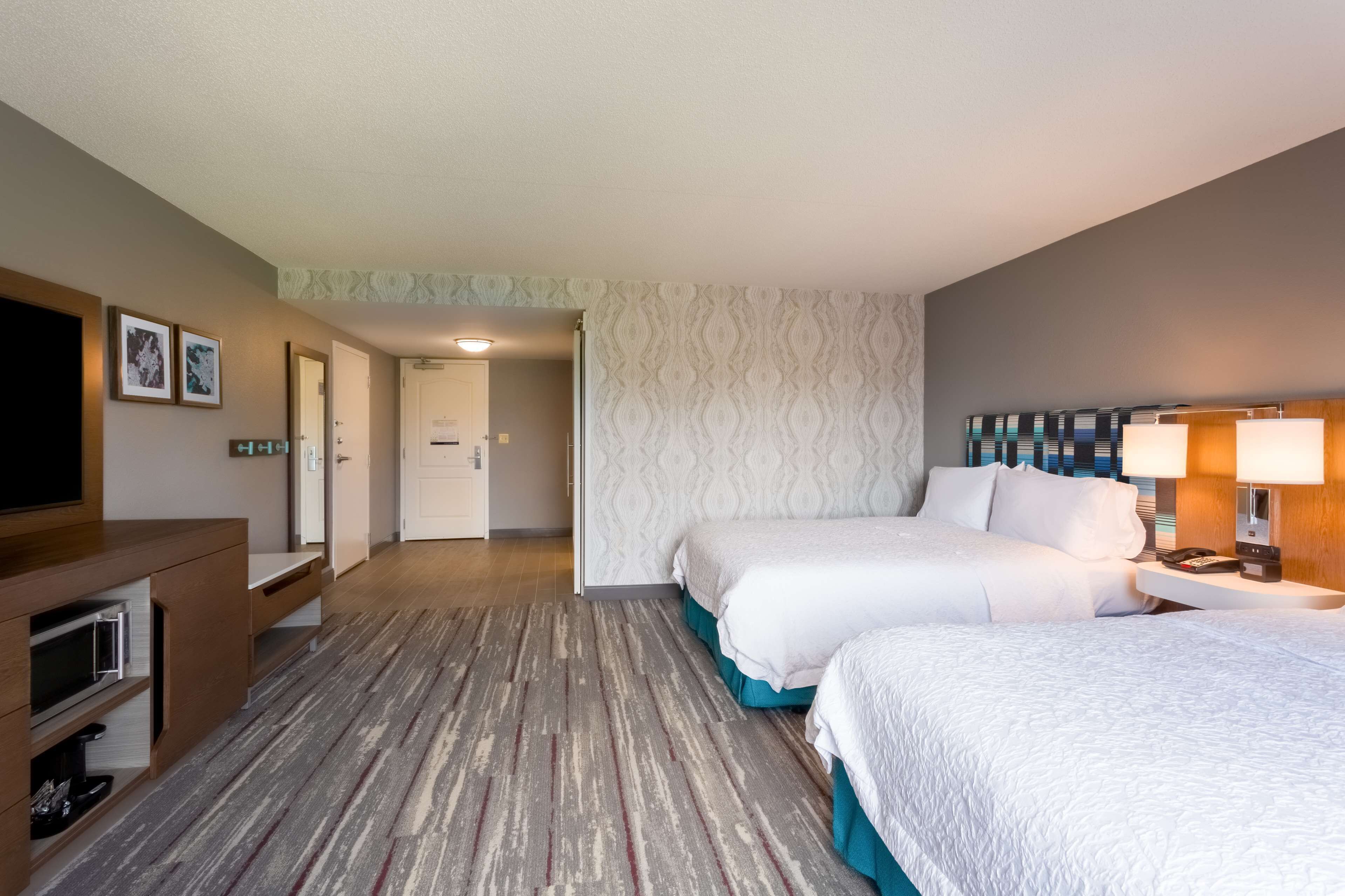 A hotel room with two beds, a TV, a desk, and a lamp.