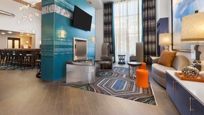 A modern hotel lobby with a bar, seating area, and a large TV screen.