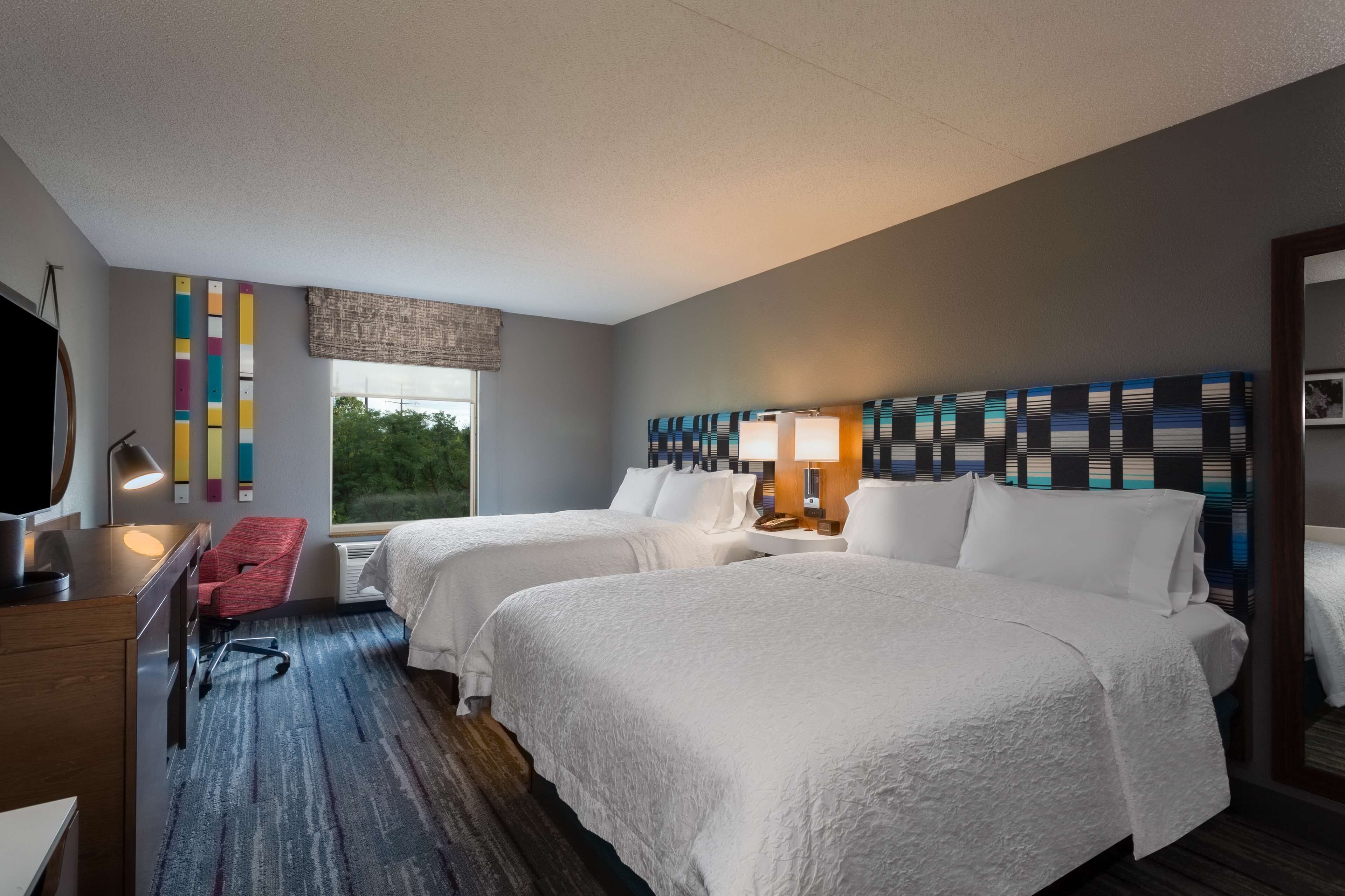 Une chambre d’hôtel avec deux lits, un bureau, une chaise et une grande fenêtre.