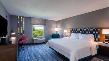 Una habitación de hotel moderna con una cama grande, un escritorio con computadora, una silla, un ventanal con vista y un cabecero estampado.