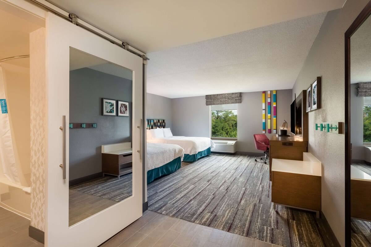 A modern hotel room with a large bed, a desk, a chair, and a view of the outdoors.