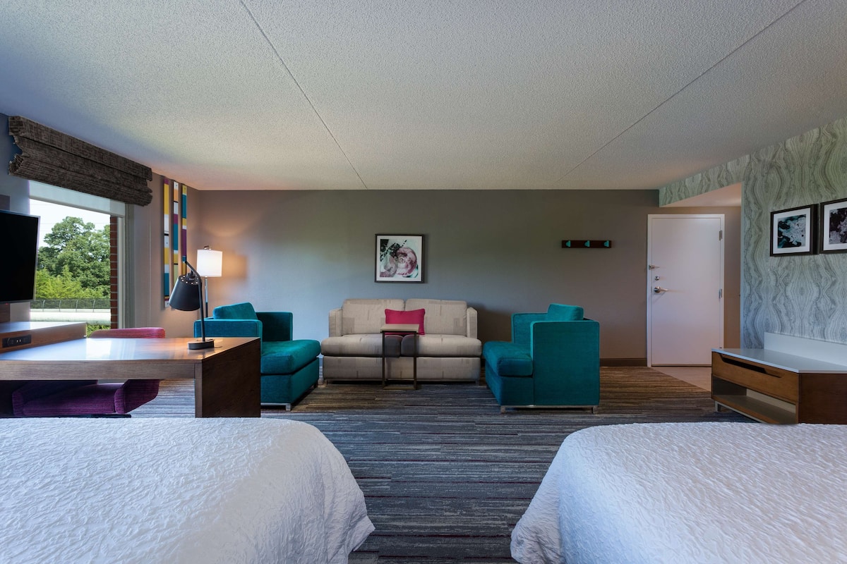 A hotel room with two beds, a sofa, a desk, and a TV.