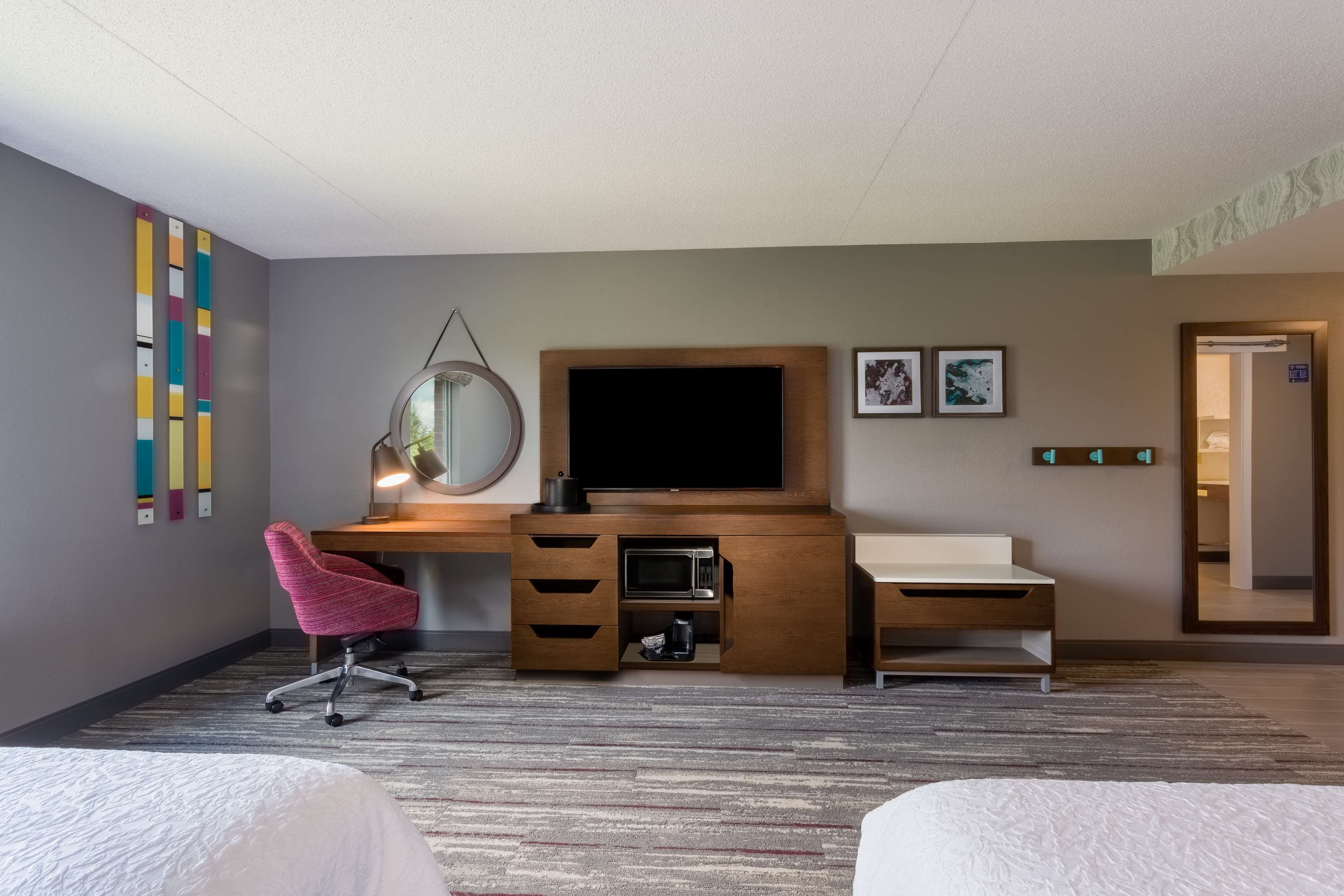 A hotel room with a bed, a desk with a computer, a TV, a mirror, and a small kitchenette.