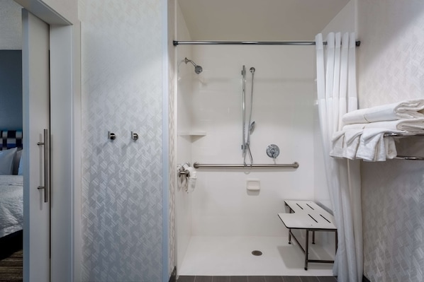 A modern bathroom with a shower, a towel rack, and a bench.