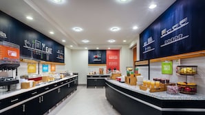 A modern breakfast area with a counter displaying various food items and a wall with promotional banners.