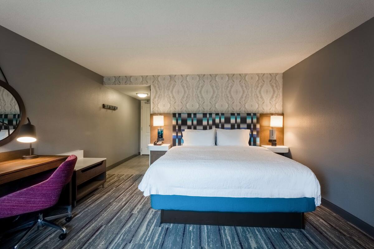 A hotel room with a large bed, a desk with a chair, and two bedside lamps.