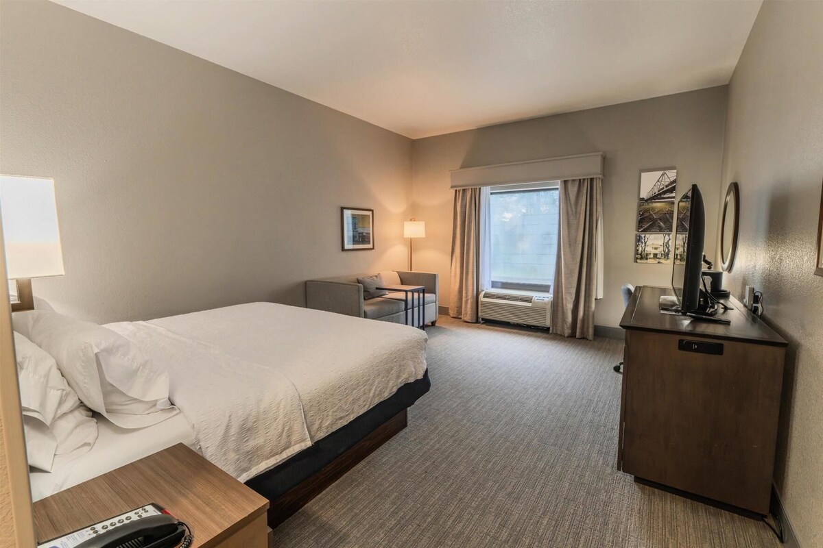 A hotel room with a bed, bedside table, desk, chair, and a television on a cabinet.