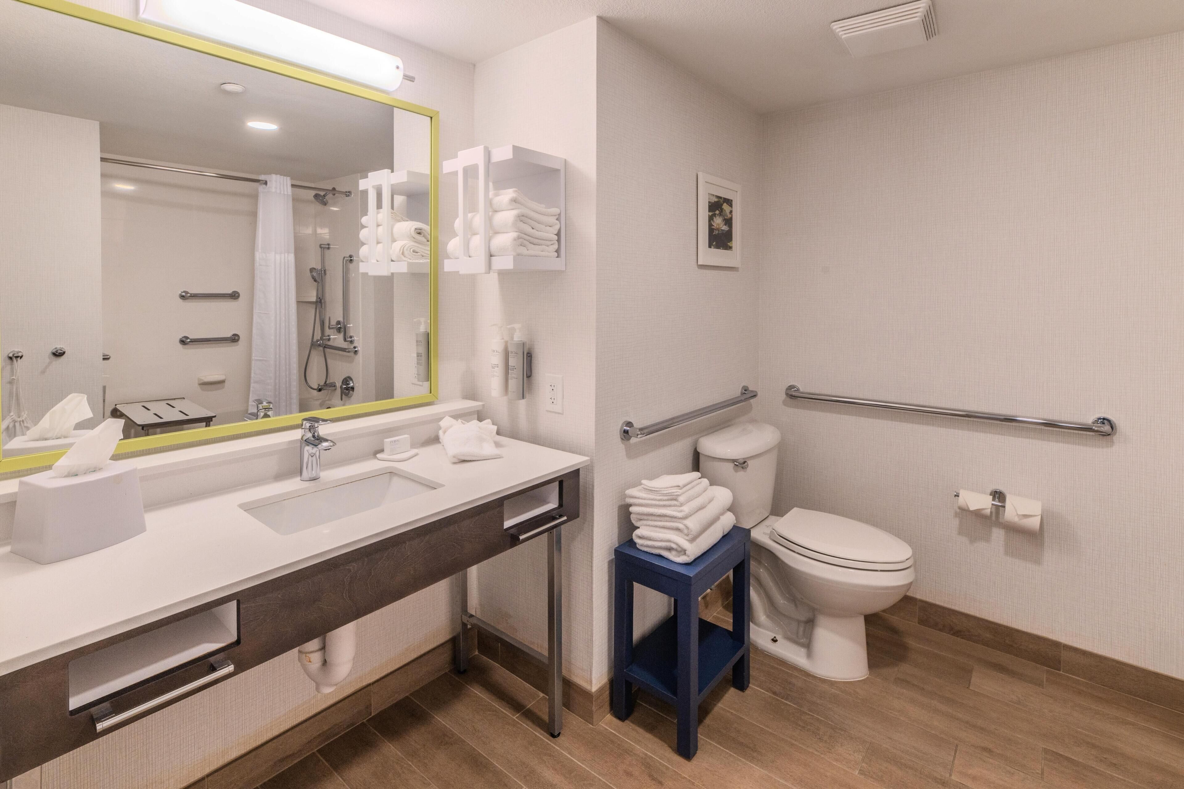 A modern bathroom with a large mirror, white sink, and a toilet with a grab bar.