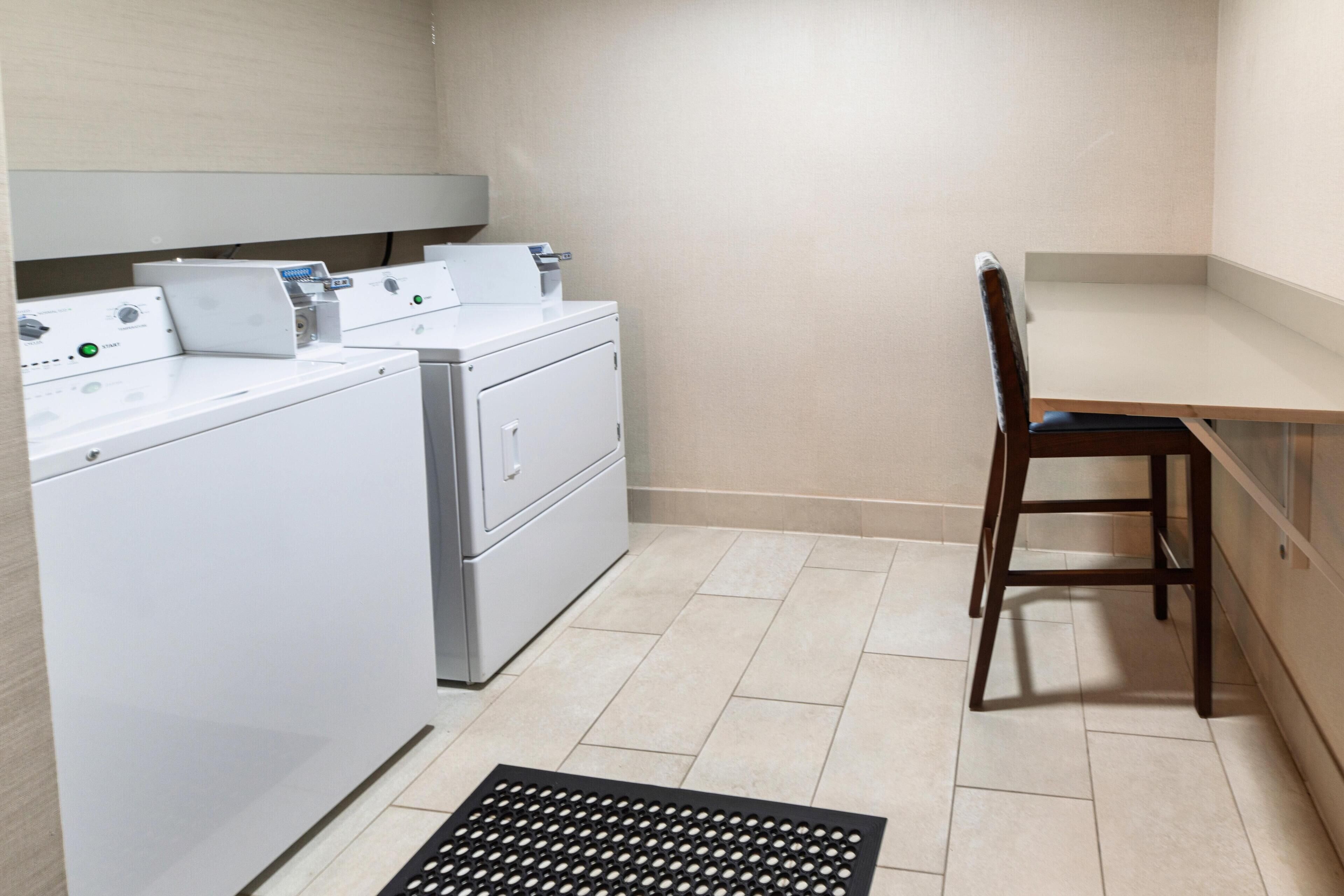 A laundry room with a washing machine, dryer, and a chair.
