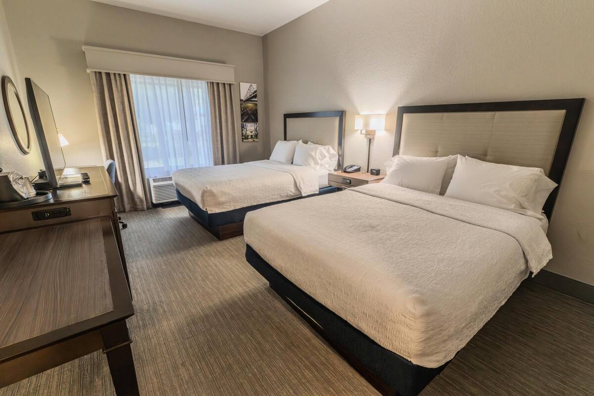 A hotel room with two beds, a desk with a telephone, a lamp, and a window with curtains.
