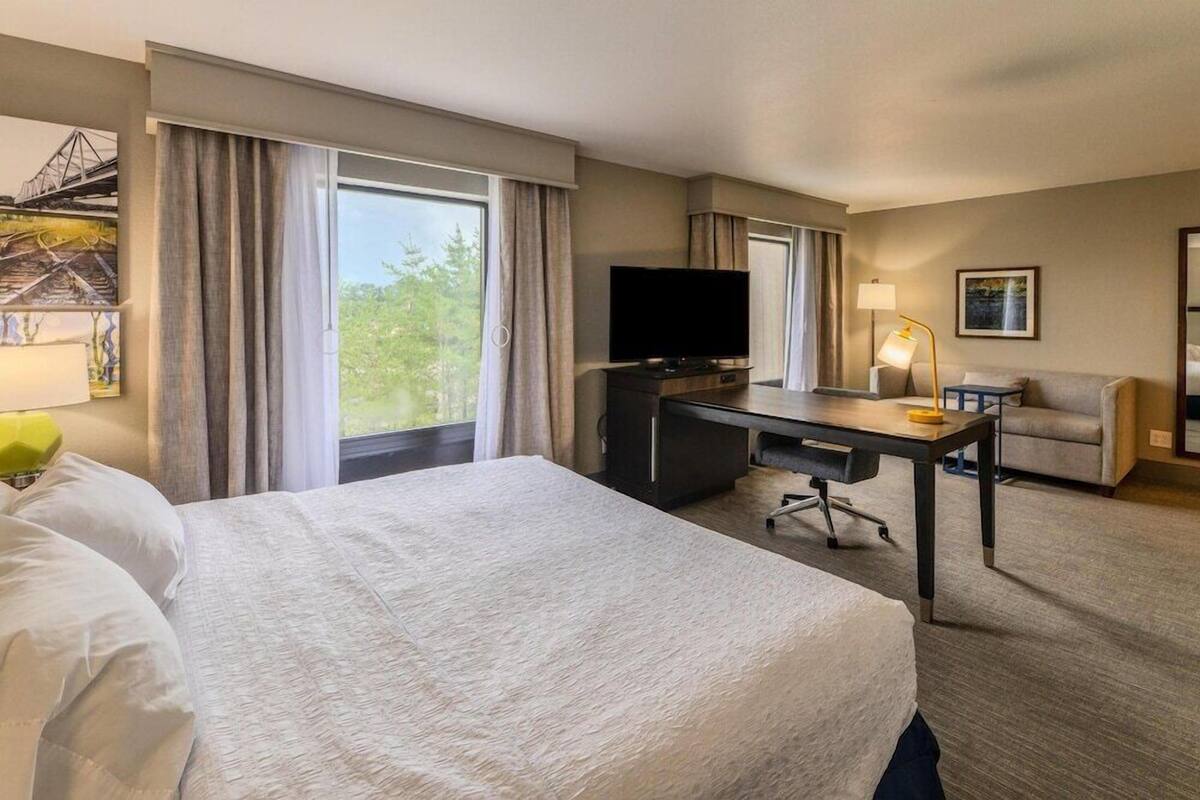 A hotel room with a bed, a desk, a television, a lamp, and a couch.