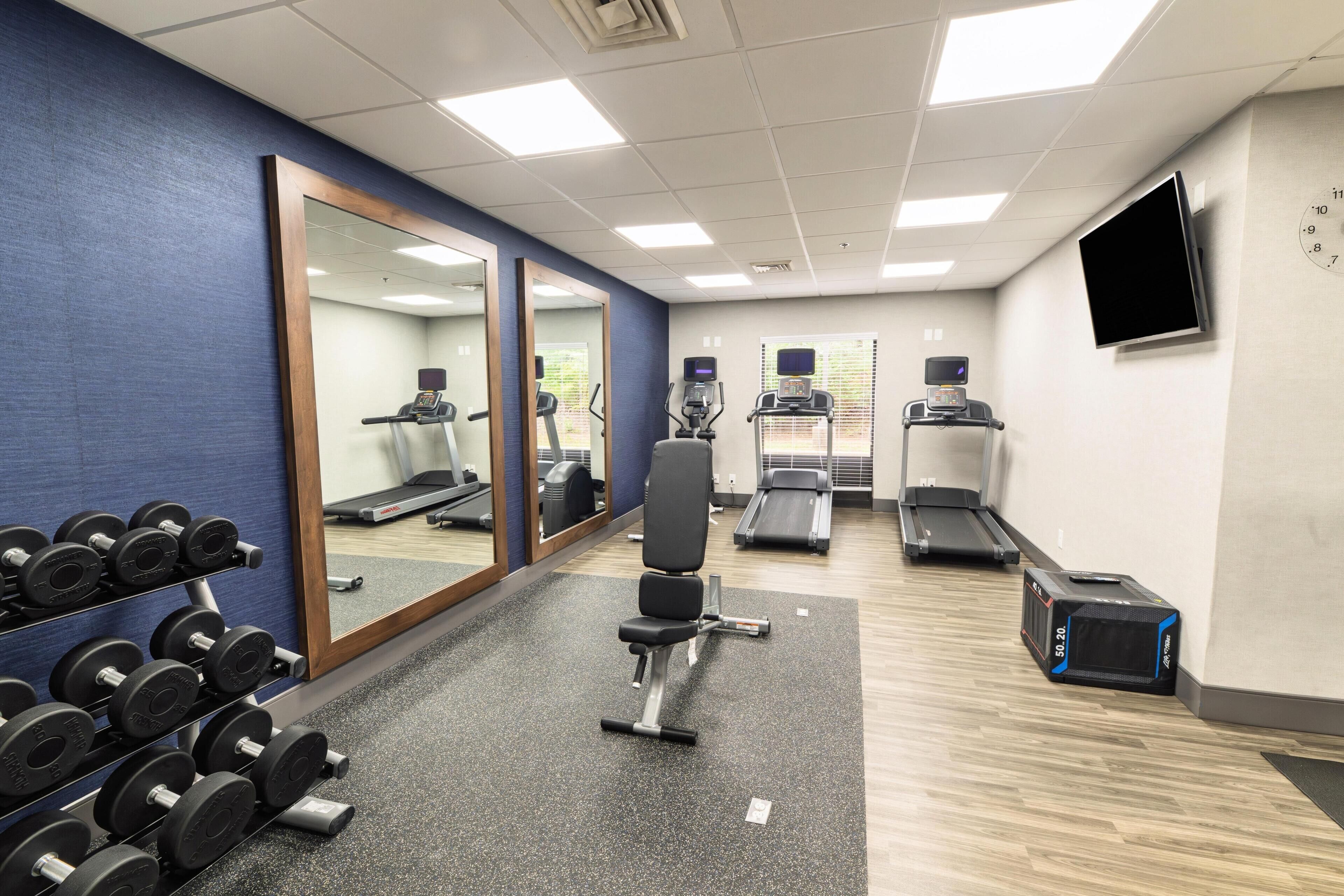 A gym with exercise equipment, a mirror, and a TV on the wall.