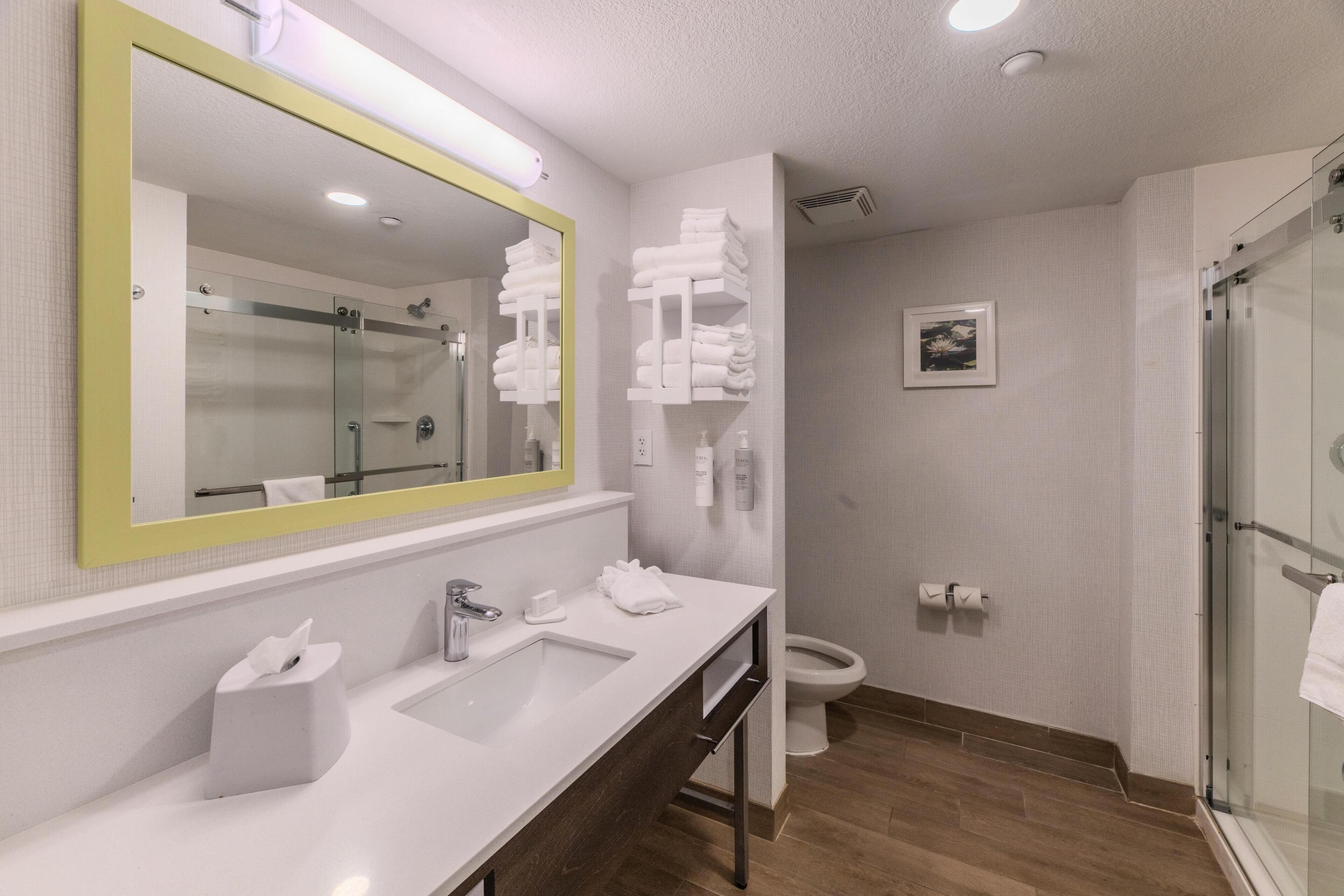 A modern bathroom with a large mirror, a sink, a toilet, and a shower.