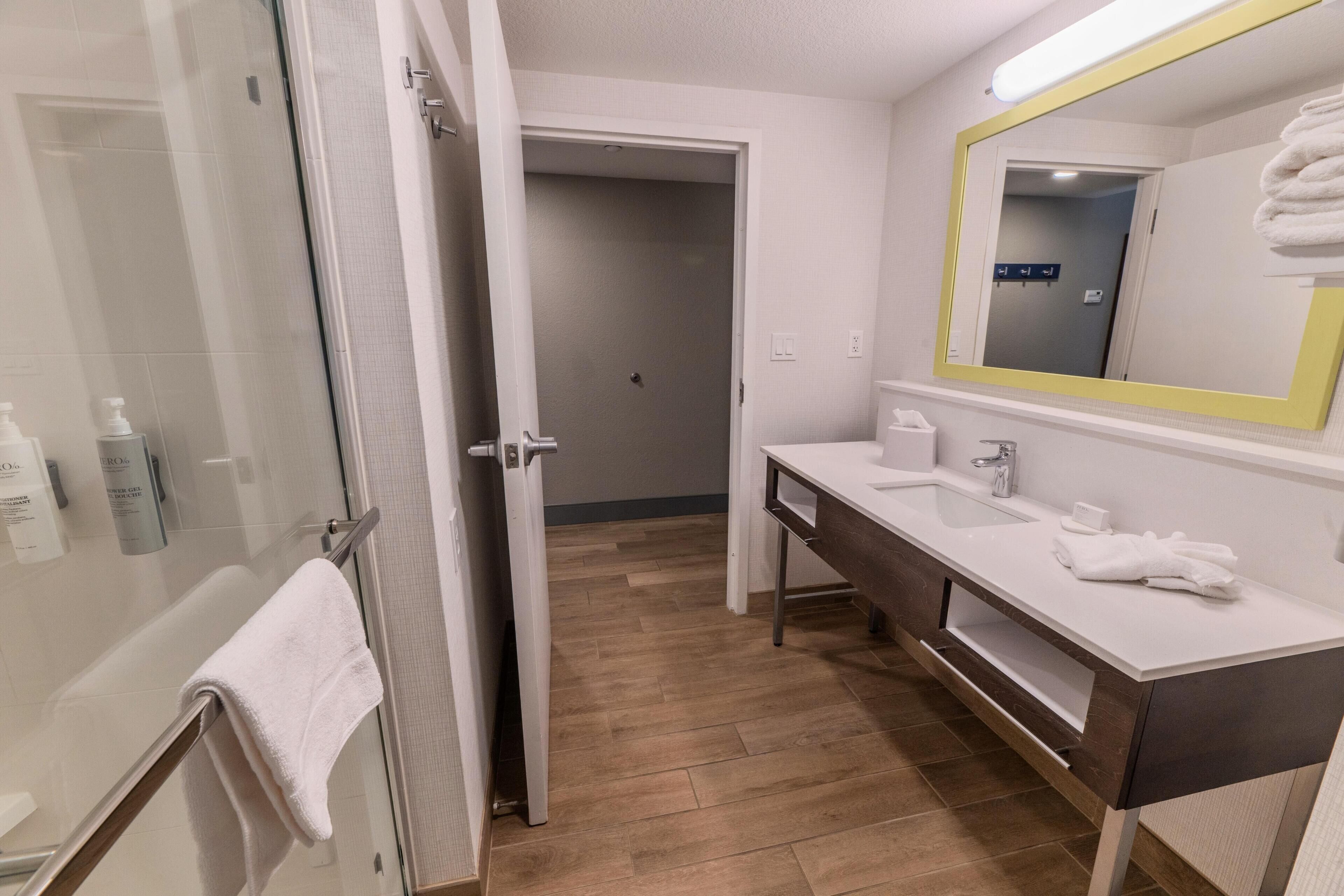 A modern bathroom with a glass shower enclosure, a white sink with a dark countertop, and a mirror with a yellow frame.