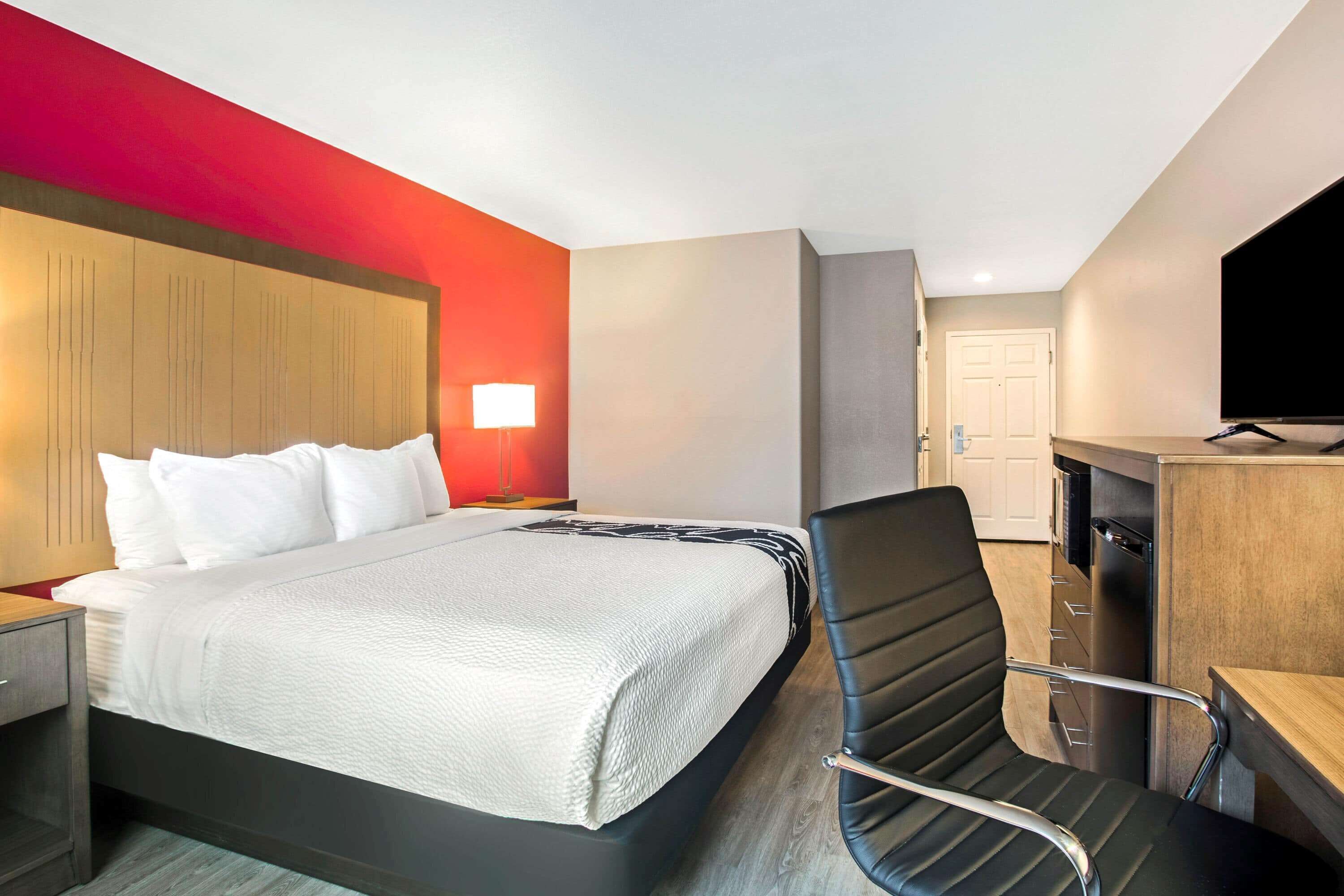Ein Hotelzimmer mit Bett, Schreibtisch, Stuhl, Fernseher und einer Tür.