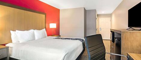 Ein Hotelzimmer mit Bett, Schreibtisch, Stuhl, Fernseher und einer Tür.