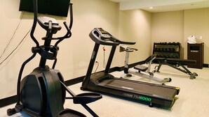 Un gimnasio con cintas de correr, una máquina elíptica y una banca de pesas.