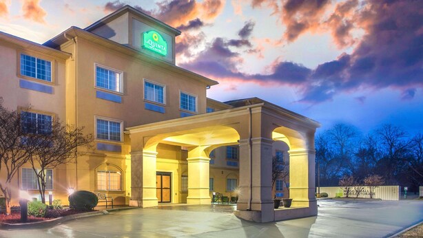 Un hotel con una entrada amplia, un letrero que dice "La Quinta", y un cielo despejado con nubes.