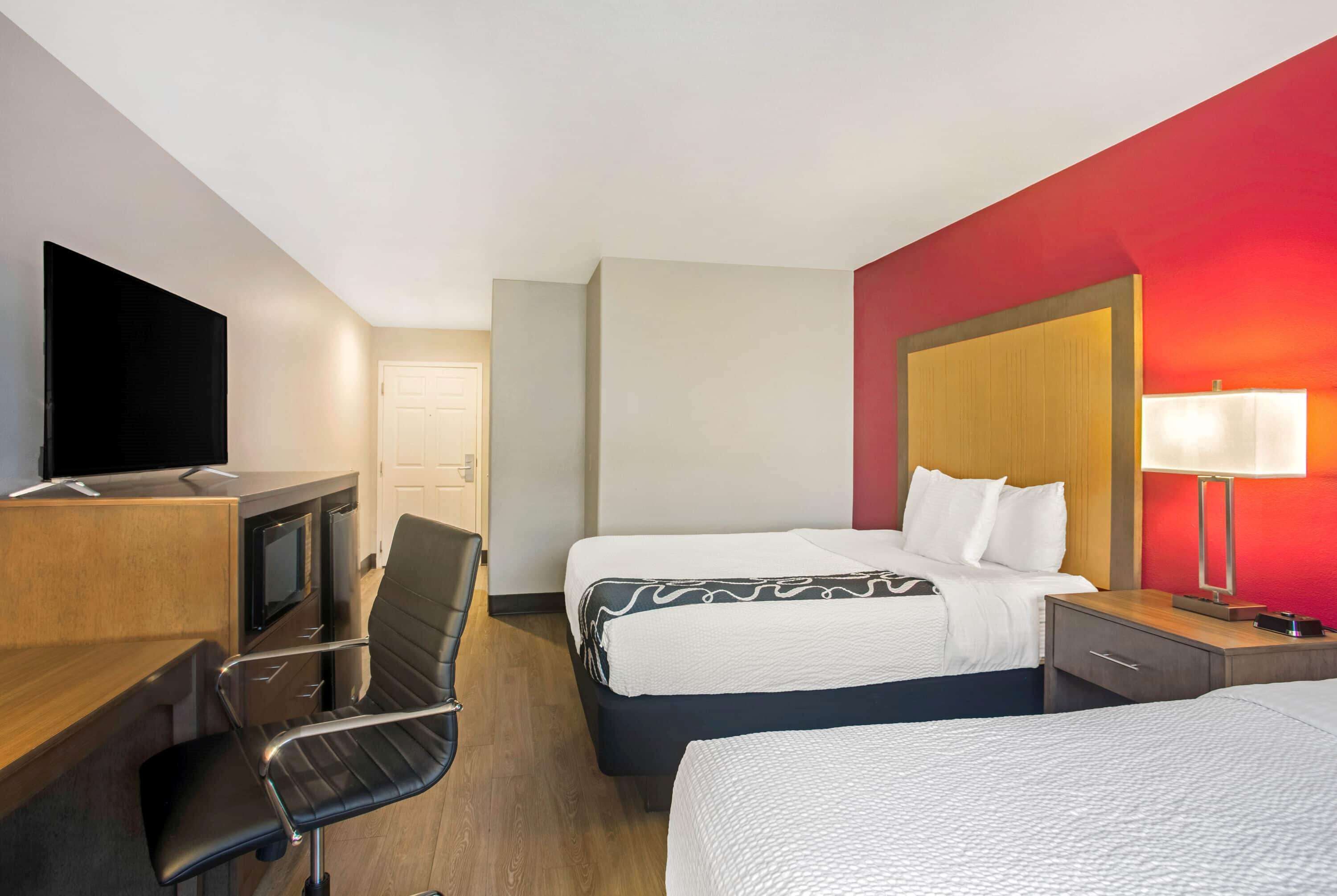 A hotel room with a desk, two beds, a TV, and a lamp.