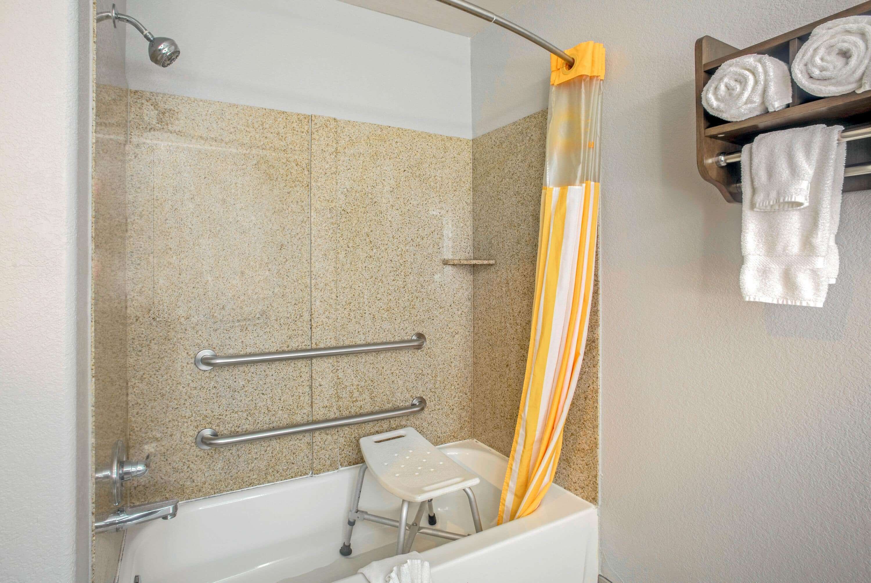 Ein Badezimmer mit Dusche, Haltegriffen, einer Trittstufe und einem Handtuchhalter mit Handtüchern.