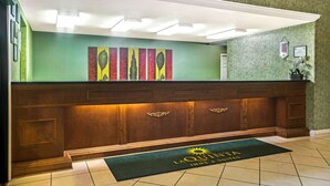 Zona de recepción de un hotel con un mostrador de madera, un cuadro abstracto de colores sobre él y un felpudo con el nombre del hotel.