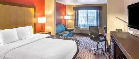 Ein Hotelzimmer mit einem großen Bett, einem Schreibtisch mit Fernseher, einem Sessel und einem Sofa.