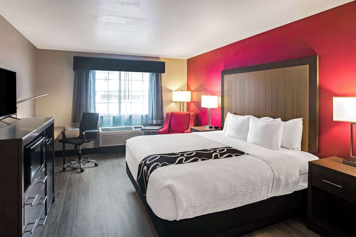 A hotel room with a large bed, a desk with a chair, a TV, and two lamps.