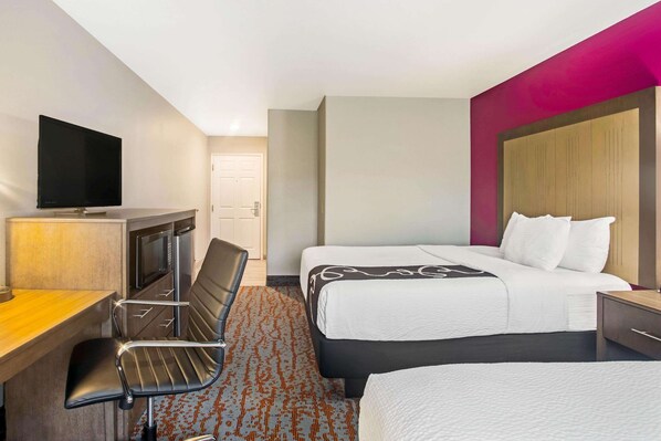 A hotel room with a bed, a desk with a chair, a television, and a door.