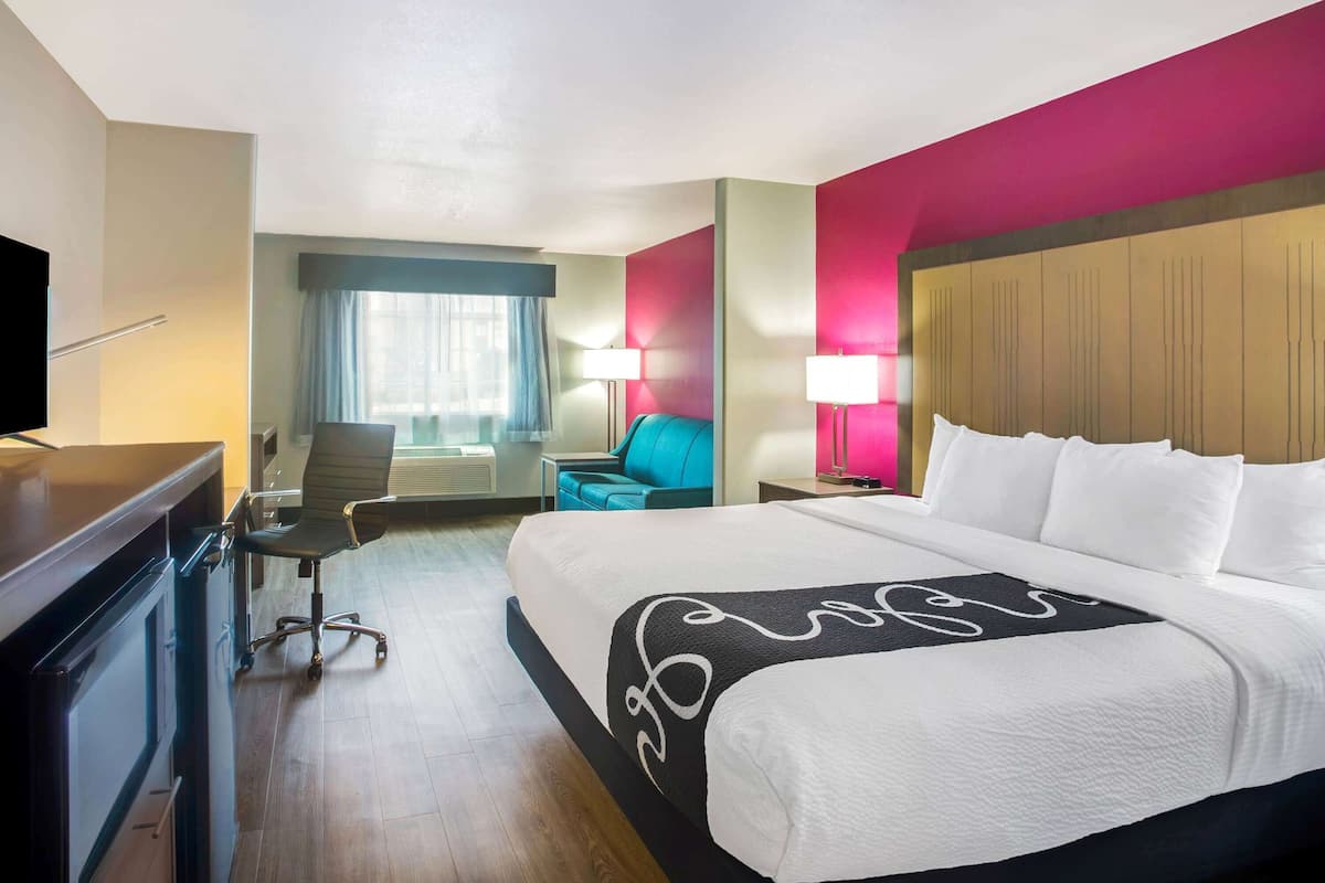A hotel room with a large bed, a desk, a chair, a TV, and a window with curtains.