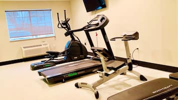 Un gimnasio con cintas de correr, elípticas y una banca.