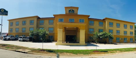 Un hotel amarillo de varios pisos con entrada central y un letrero que dice 'La Quinta Inn & Suites'.