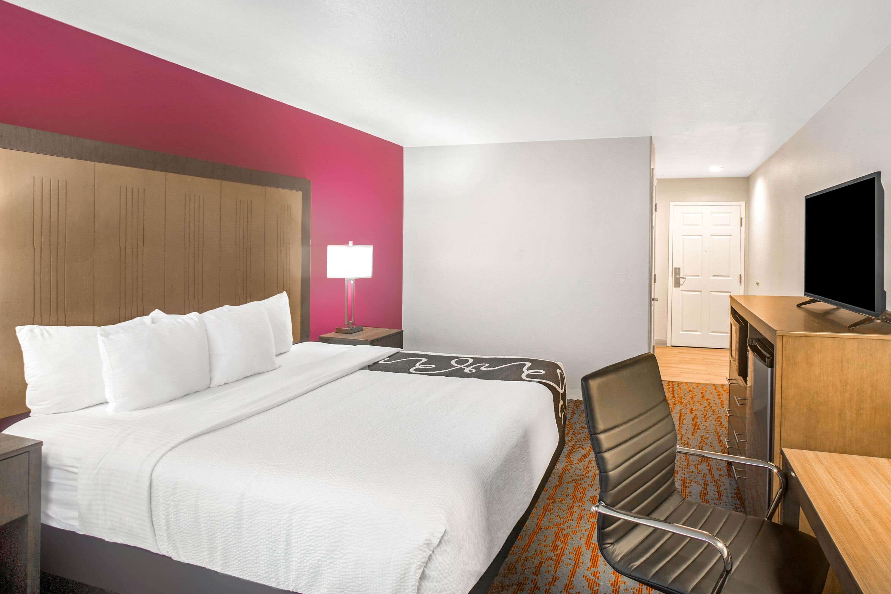 Una habitación de hotel con cama, escritorio, silla, televisor y puerta.