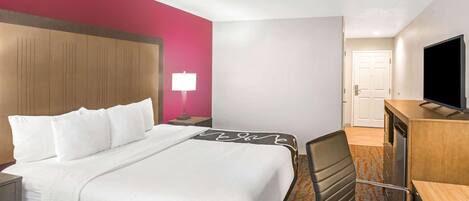 Una habitación de hotel con cama, escritorio, silla, televisor y puerta.