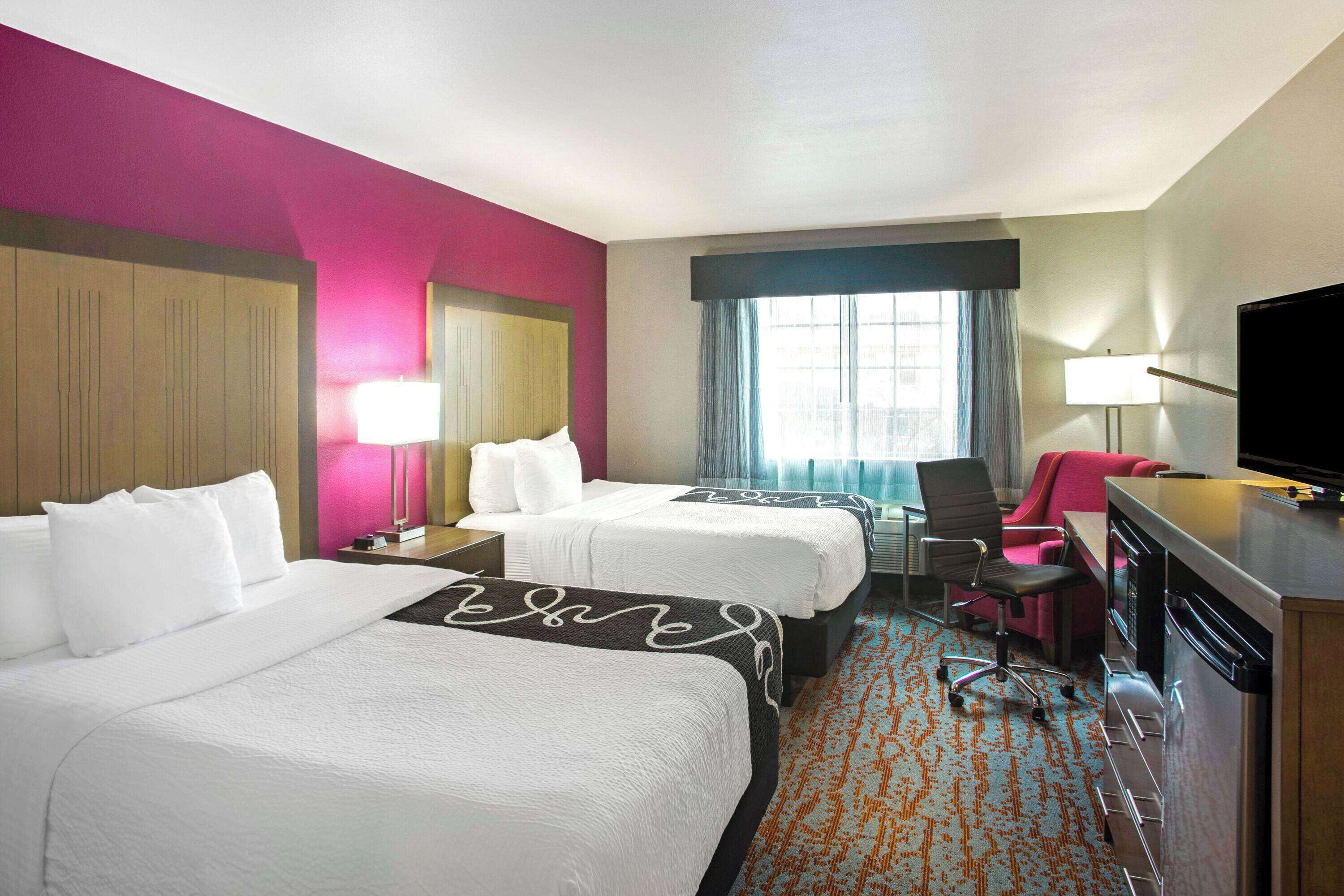 A hotel room with two beds, a desk, a chair, a TV, and a window with curtains.