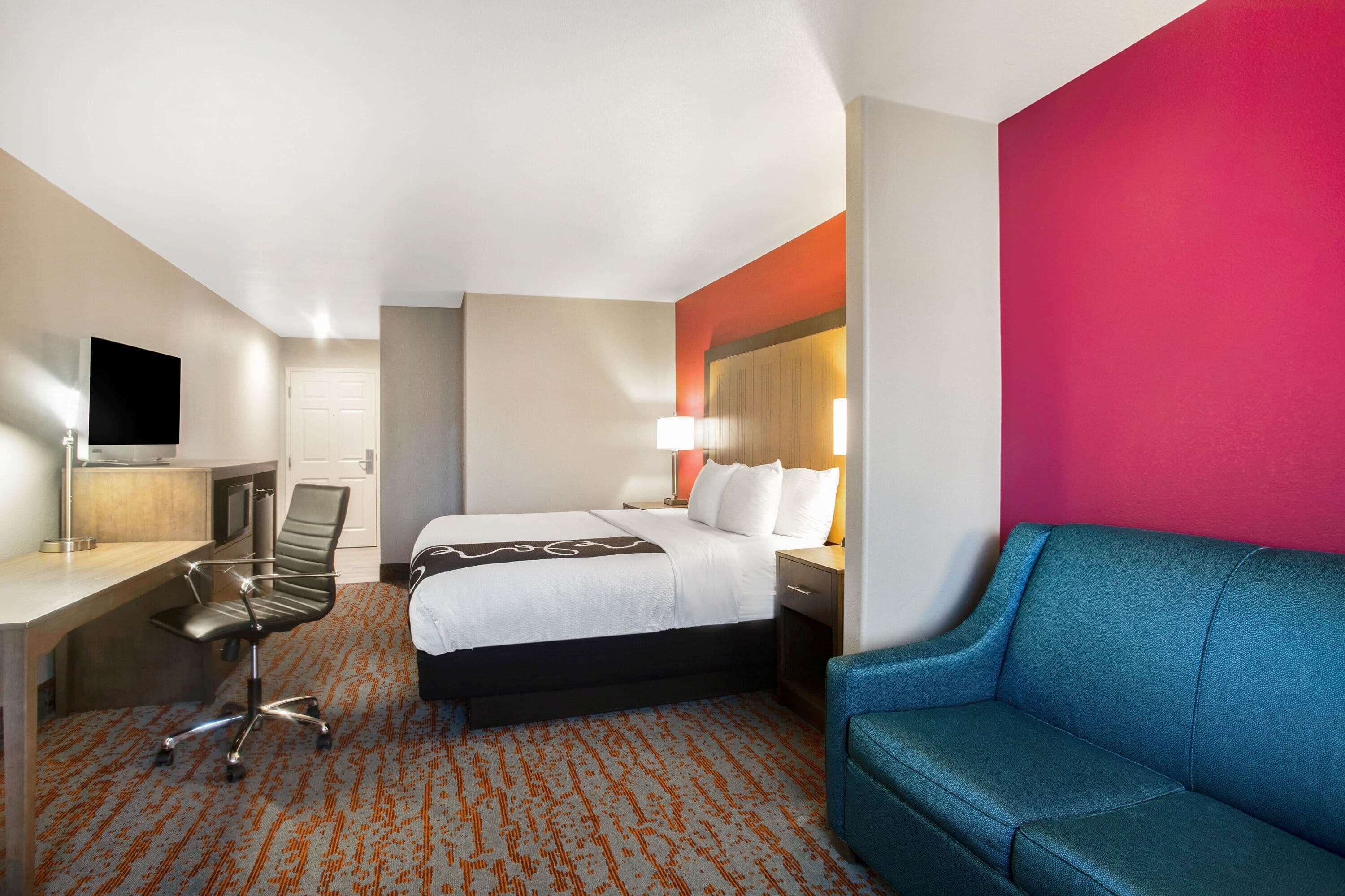 A hotel room with a bed, a desk, a chair, a TV, and a sofa.