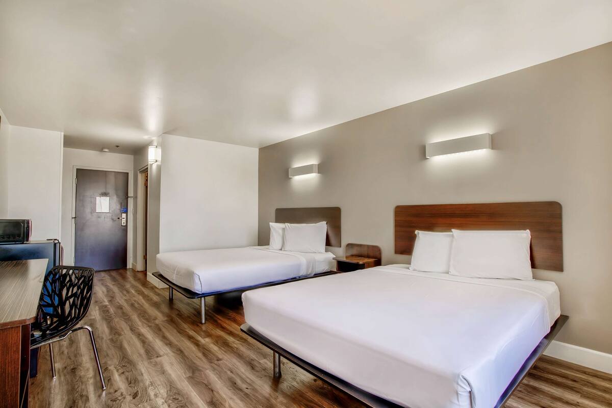 A hotel room with two beds, a desk, and a chair.