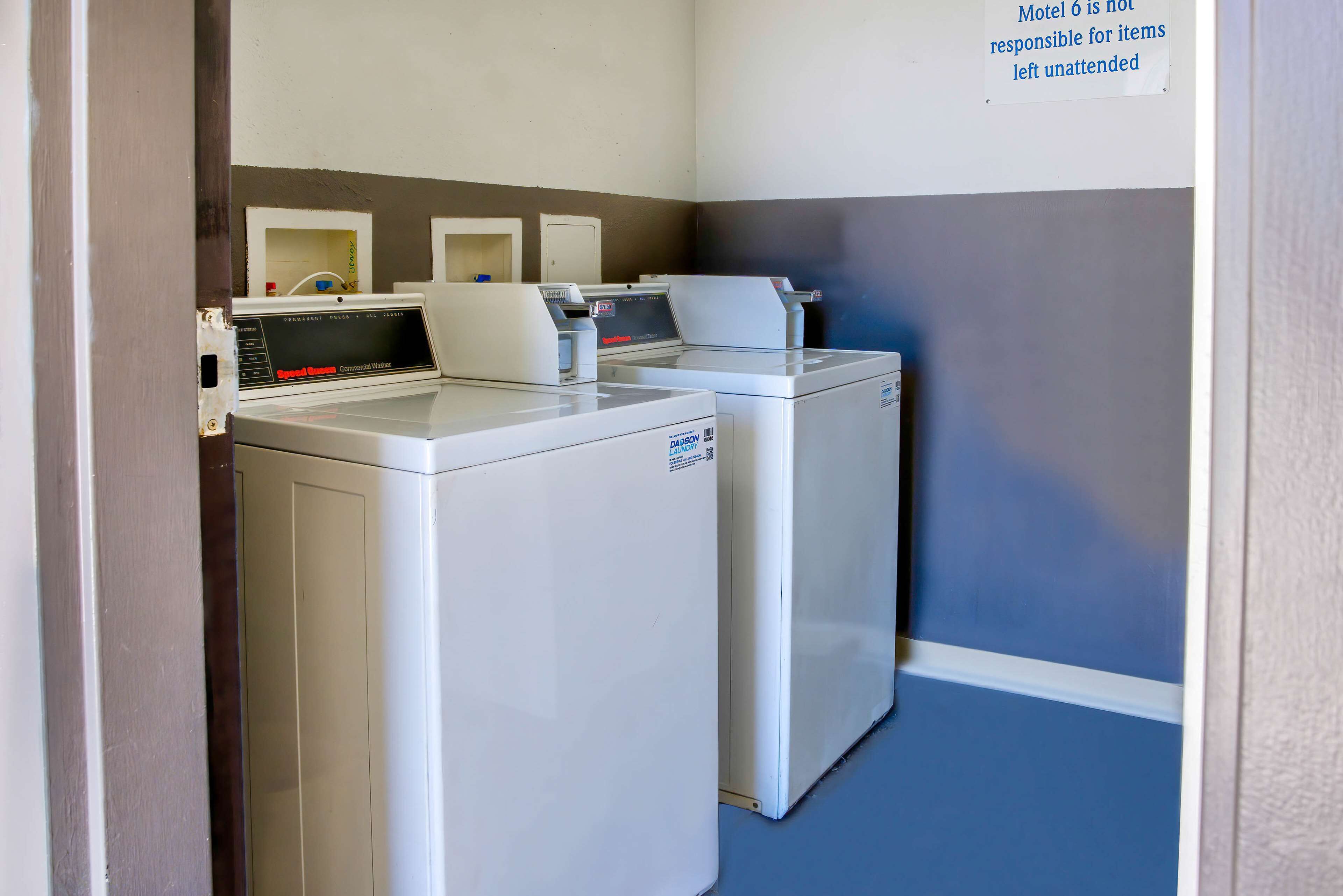 Een wasserijruimte met twee voorladers wasmachines en drogers, een bordje met het beleid van het motel over onbeheerde spullen, en een blauwe vloer.