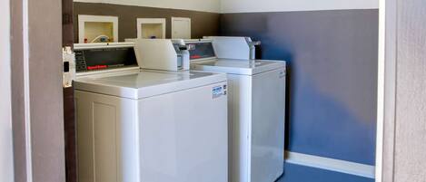 A laundry area with two front-loading washers and dryers, a sign indicating the motel's policy on unattended items, and a blue floor.