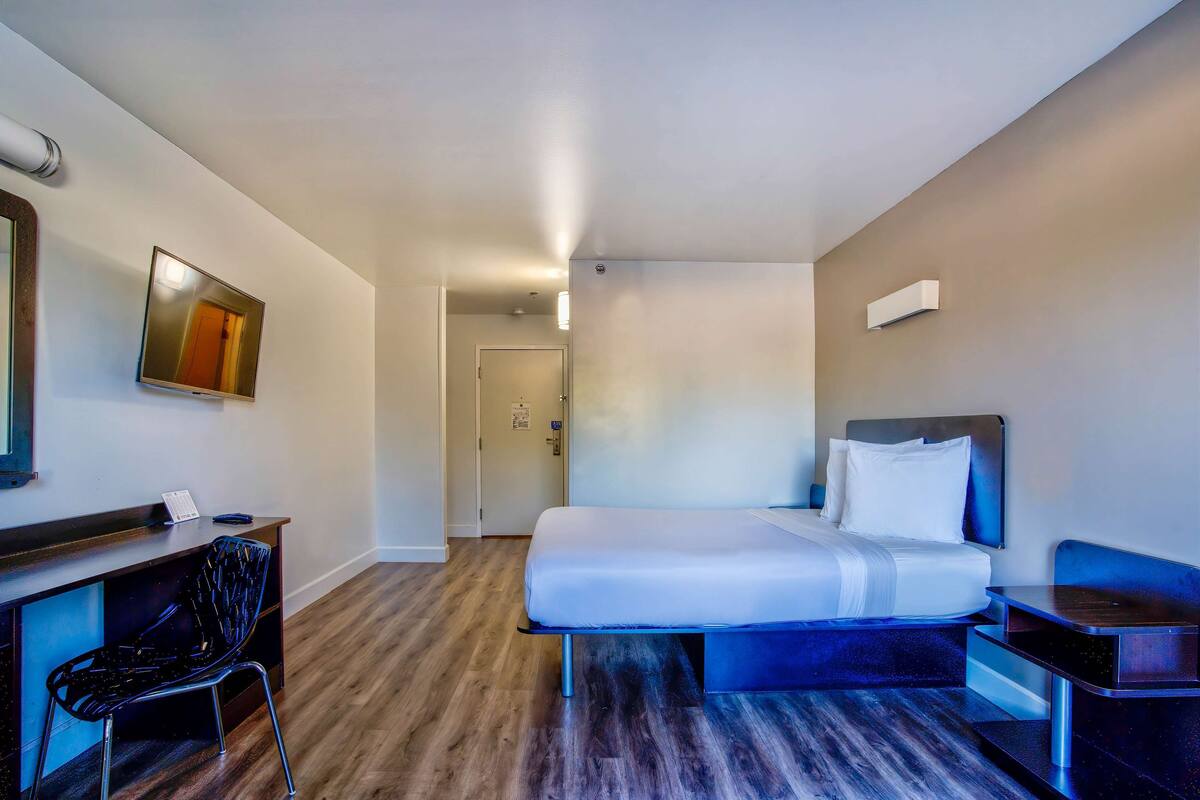 A hotel room with a bed, desk, chair, and a door leading to another room.