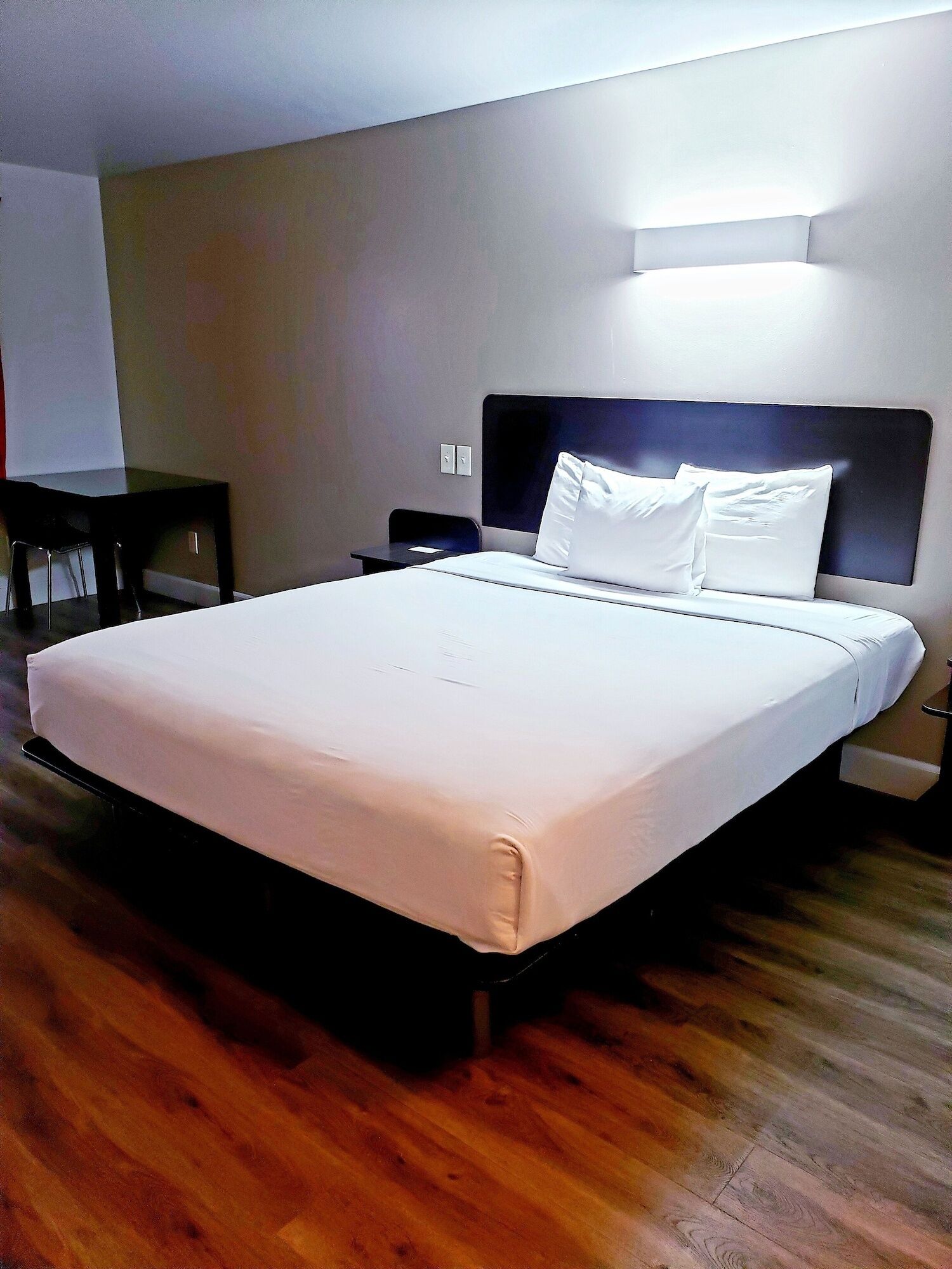 A hotel room with a large bed, a bedside table, a chair, and a desk.