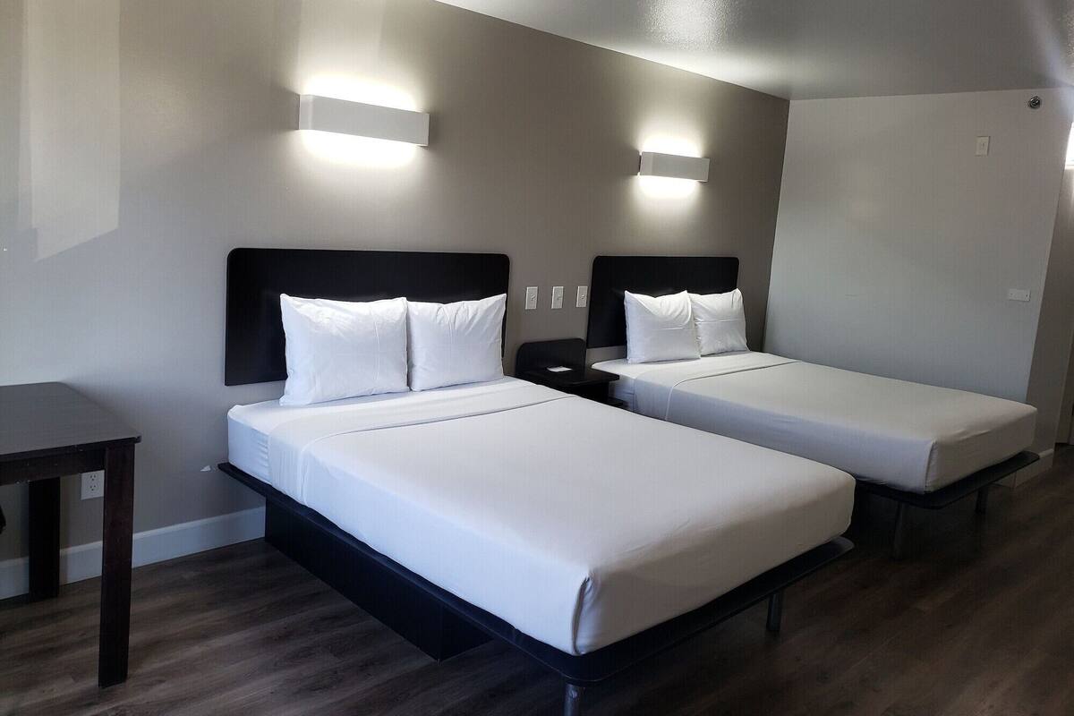 A hotel room with two single beds, a desk, and two wall-mounted lights.
