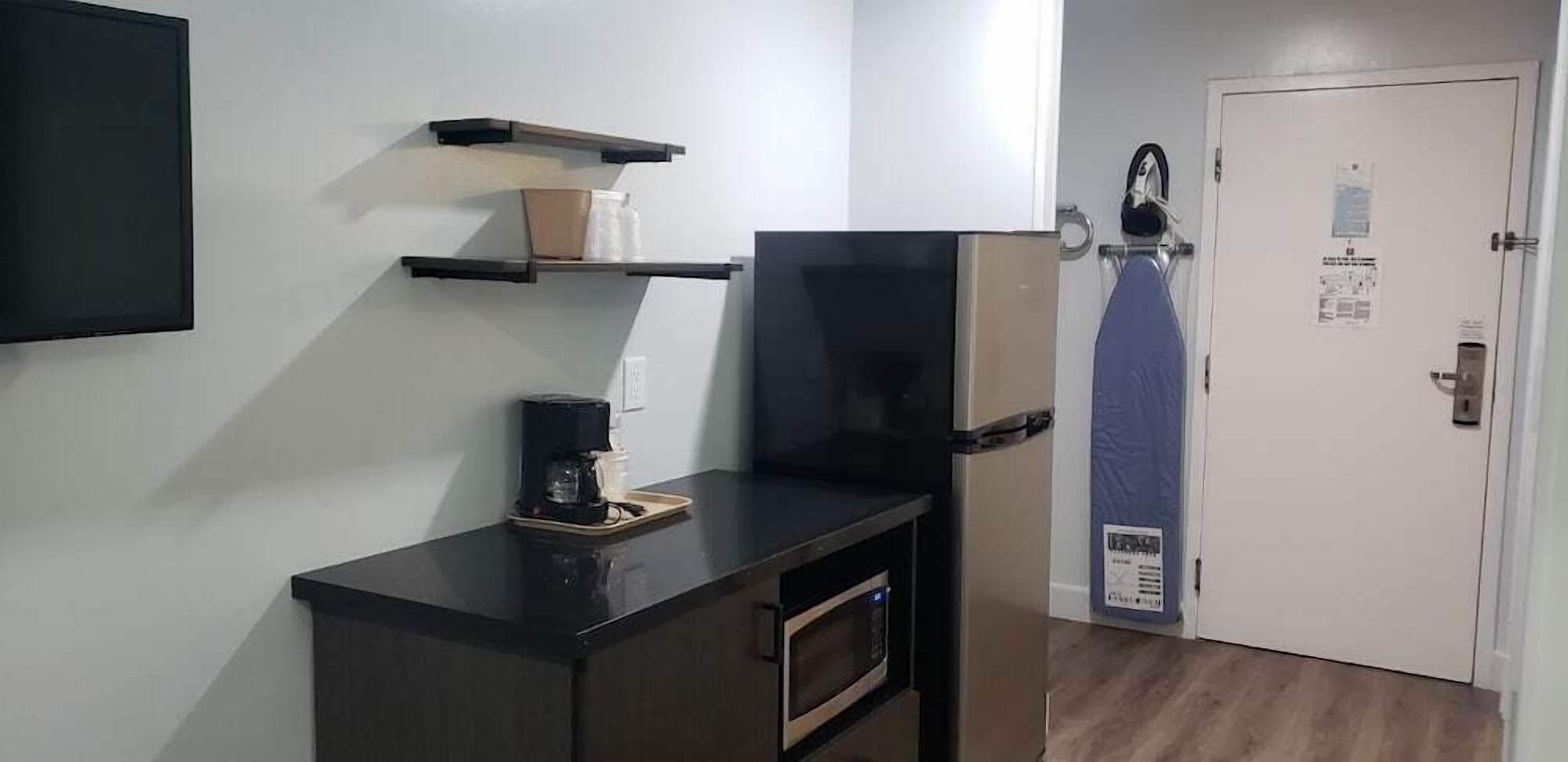 Une petite cuisine équipée d’une machine à café, d’un four à micro-ondes et d’un réfrigérateur. Des étagères murales sont fixées au-dessus du plan de travail.