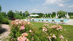 Un área de piscina con sillas de descanso y sombrillas, rodeada de abundante follaje y plantas en flor.