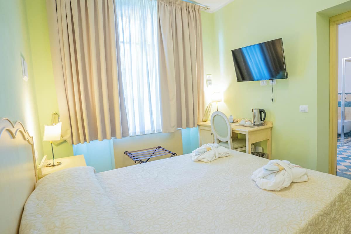 Habitación de hotel con cama, escritorio con espejo, televisor y baño visible a través de una puerta abierta.
