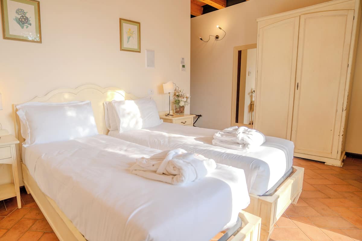 Habitación de hotel con dos camas, una mesita de noche con lámpara, un armario y un espejo.