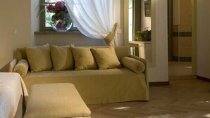Una habitación con un sofá color beige, un reposapiés a juego y una ventana con cortinas translúcidas.